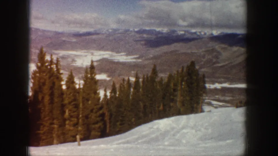 1961 Aspen-area 8mm frame showing a snow-covered hillside, evergreen forest, and distant mountain valley.