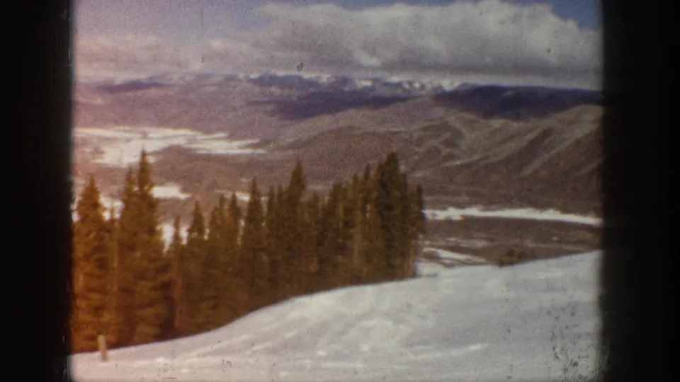 1961 Aspen-area 8mm frame with a bright snowfield, evergreen stand, broad valley, and distant mountain ridges.