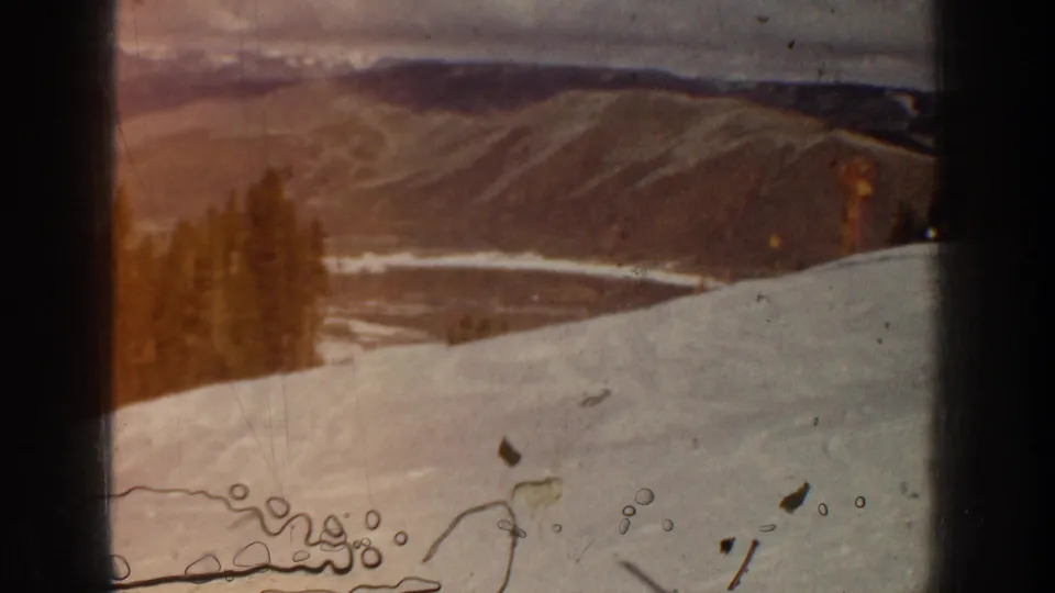 Faded 8mm frame from the 1961 Aspen ski setting, with a snowy foreground, trees, distant hills, and pronounced film artifacts.