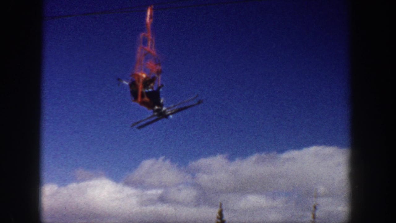 In 1961 Aspen, Colorado footage, a red chairlift carries a skier over snow with clouds low on the horizon.