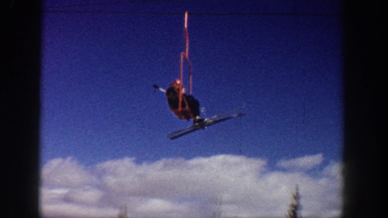 A skier sits on a red chairlift against blue sky and clouds above the slope.