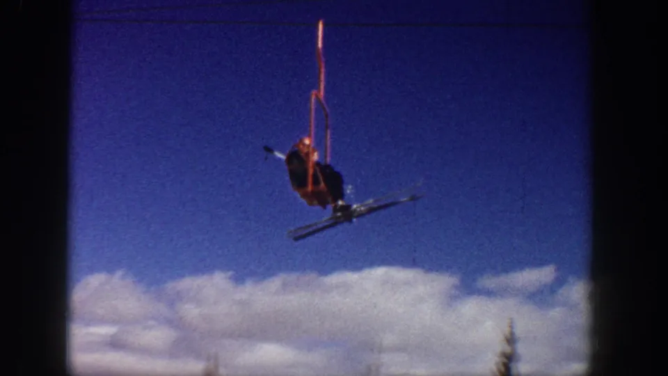 A red chairlift with a skier passes across the sky in archival Aspen ski footage from 1961.