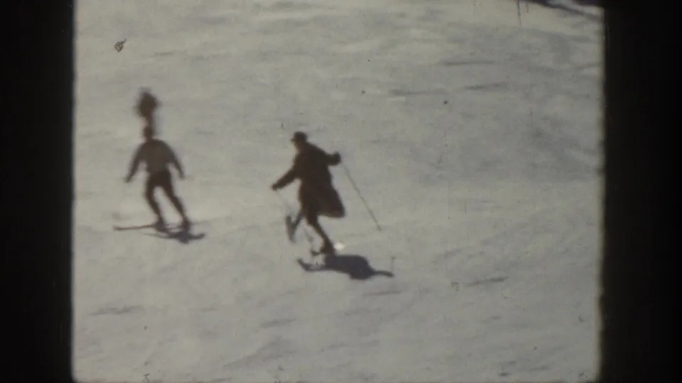 Two skiers in winter clothing descend an Aspen snow slope in 1961 home-movie footage.