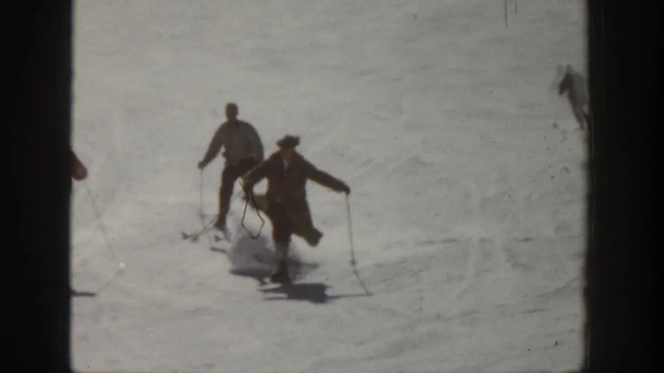 A small group of skiers in coats and hats moves downhill on an Aspen slope in 1961 footage.