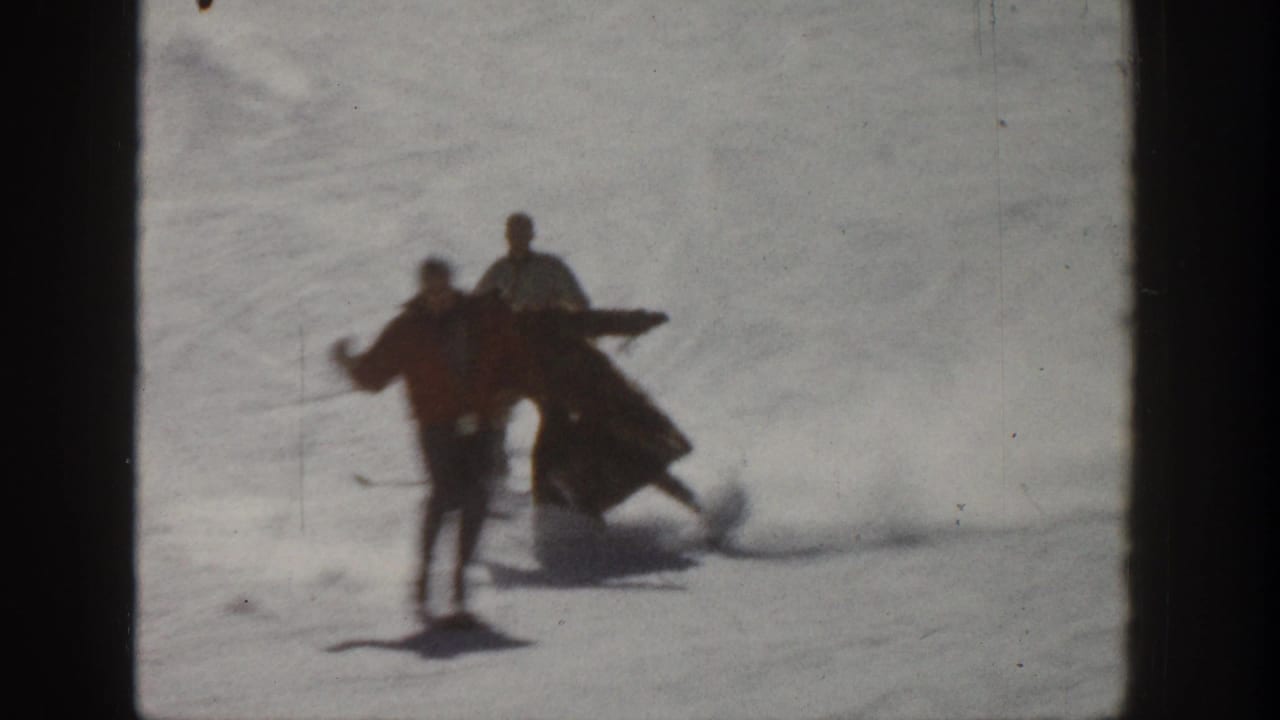 1961 Aspen home-movie frame of adults on skis on a snowy slope, including one skier appearing to lose balance beside two standing skiers.