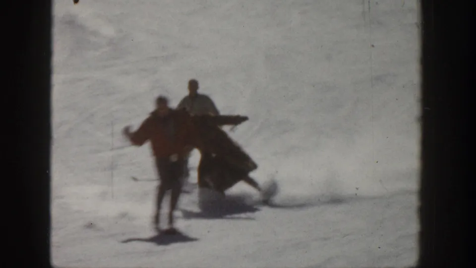 1961 Aspen home-movie frame of adults on skis on a snowy slope, including one skier appearing to lose balance beside two standing skiers.