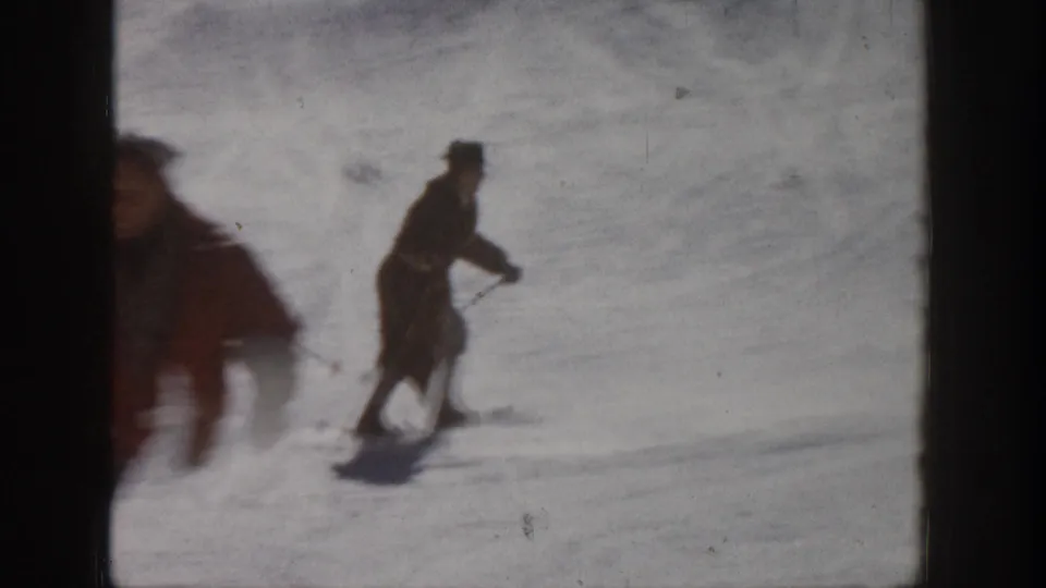 1961 Aspen ski footage with a distant adult skier crossing the snow and a motion-blurred skier passing close to the lens.