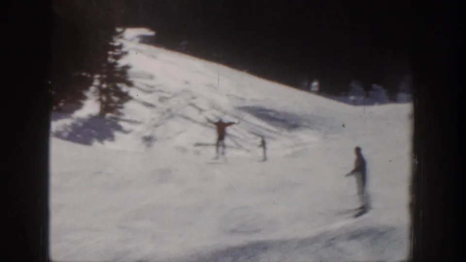 1961 Aspen home-movie frame showing distant skiers on a bright snowy slope with trees at the edge.