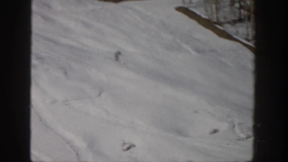 Aspen, Colorado 1961 frame with a lone distant skier crossing a pale snowy hillside below trees.
