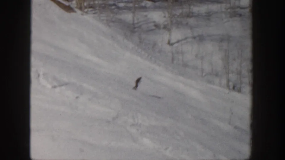 1961 Aspen frame with a lone skier carving across the snow while bare aspen trunks line the upper slope.