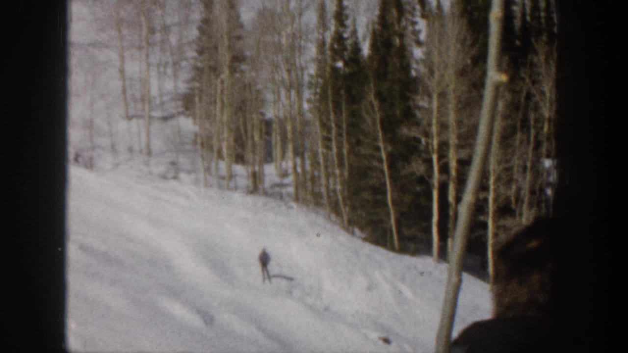 1961 Aspen 8mm frame with a lone skier moving across a snowy mountain slope lined with aspen and evergreen trees.