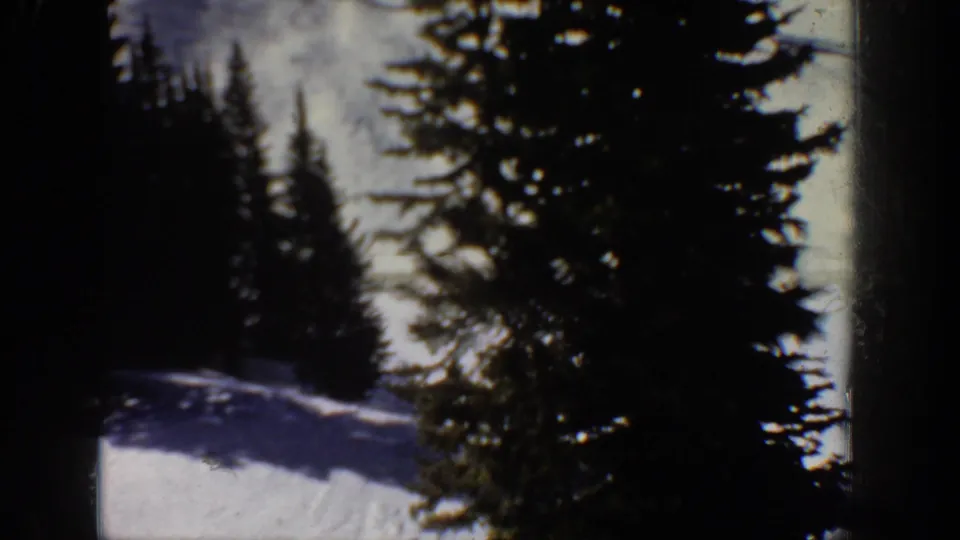 Aspen winter scene from the 1961 8mm clip, showing a snow-covered slope framed by tall evergreen trees and dark film-edge vignetting.