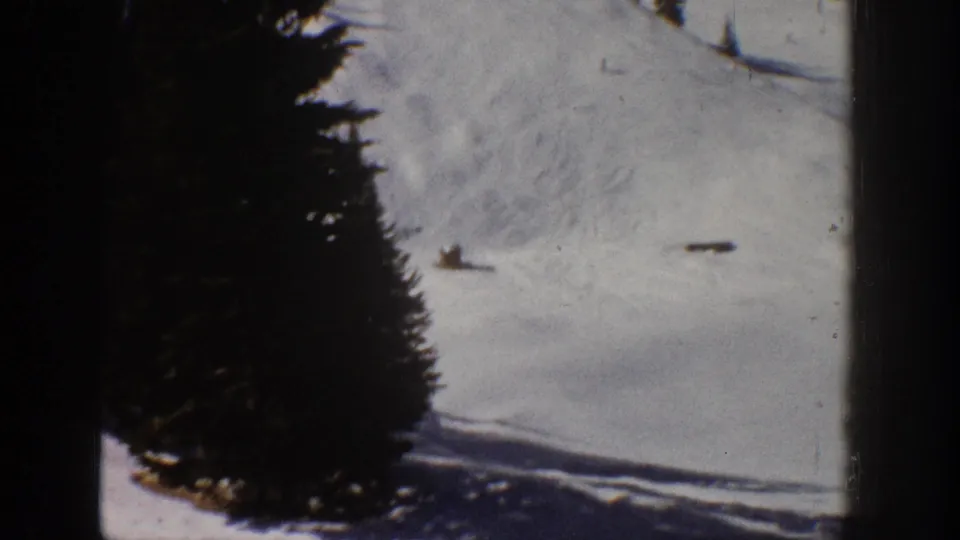 Final frame from the Aspen 1961 home movie showing a small skier on a bright snowfield, partly framed by tall evergreen trees.