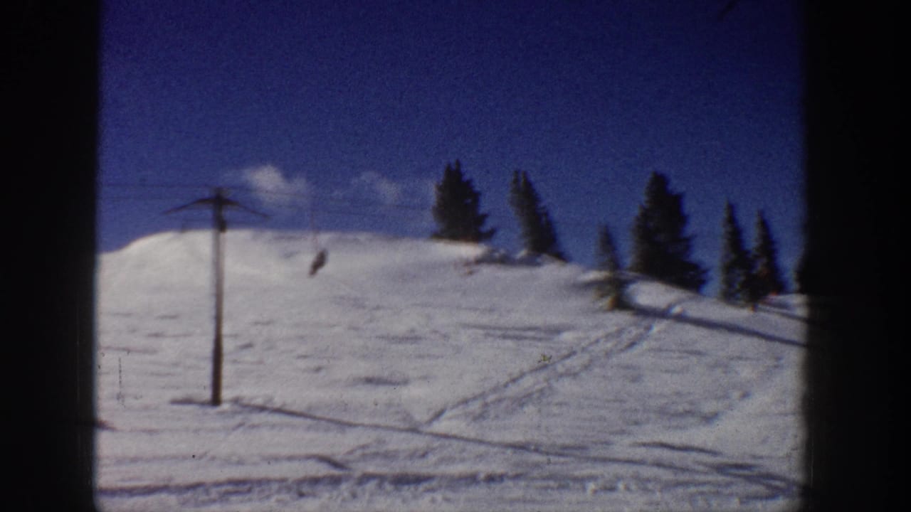 Snowy ski slope with a lift pole, cable, evergreen trees, and tracks in the snow.