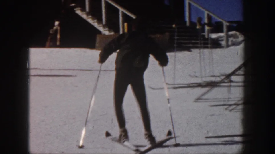A wider 1961 Aspen view shows the skier from behind using poles on a snowy surface near stairs and railings.