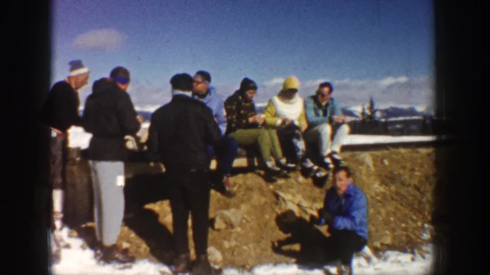 1961 Aspen frame of friends sitting and standing on a rocky mountain overlook, dressed in winter coats and ski pants.