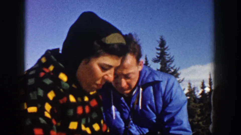 Close 1961 Aspen frame of two bundled adults, one in a patterned hooded garment and one in a blue jacket, focused on a snack or object.