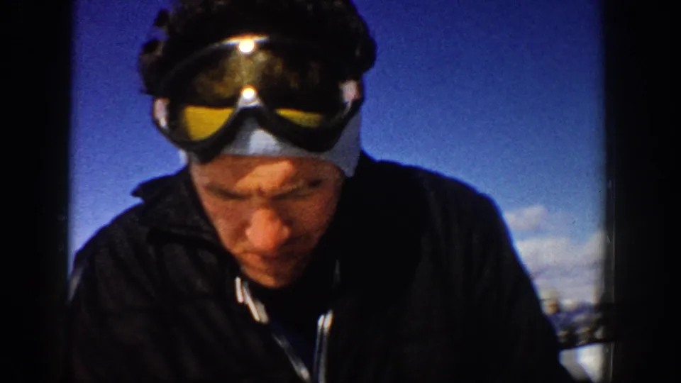 1961 Aspen home-movie close view of a man wearing ski goggles on his head, with snow and blue sky in the background.