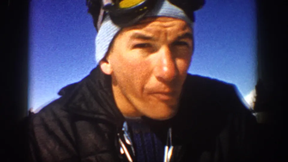 1961 Aspen frame showing a man in dark winter clothing with goggles above his forehead, filmed close to the camera outdoors.