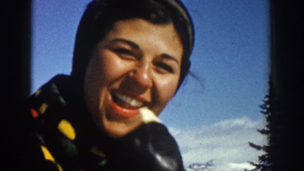 Woman smiling close to the camera against snow, sky, and dark pine trees.