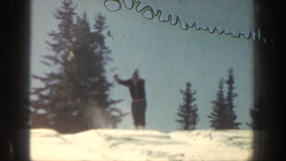 A distant skier stands or glides on snow in the Aspen landscape, framed by pines and small-gauge film edges.