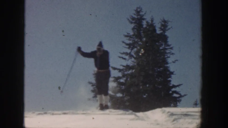 A skier moves across the snowy Aspen scene with ski poles, tall pines, blue sky, and visible 8mm film border.