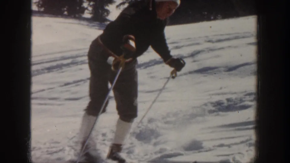 Adult skier slows or stops with poles forward on a tracked snowy slope in 1961 Aspen footage.