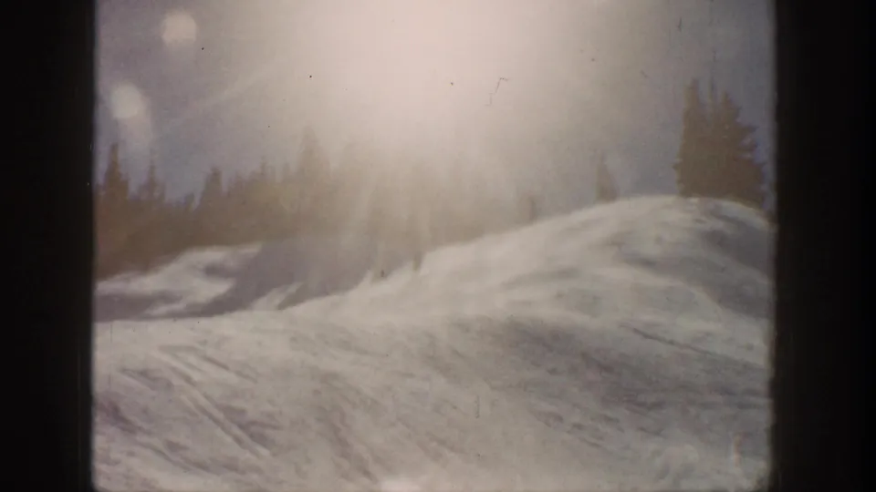 Aspen, Colorado 1961 home-movie frame showing a sunlit snow slope, tree line, lens flare, and dark film gate edges.