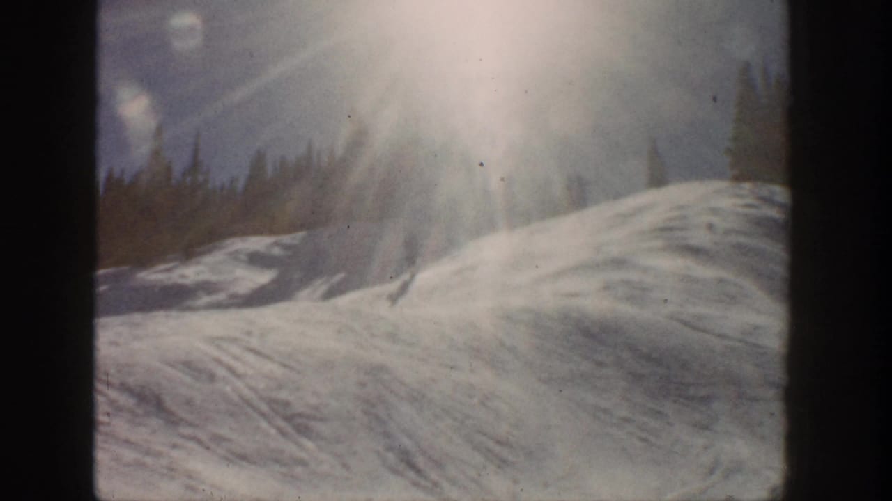Aspen, Colorado 1961 frame of a snowy hillside, intense sun glare, and evergreen tree line in soft 8mm color.