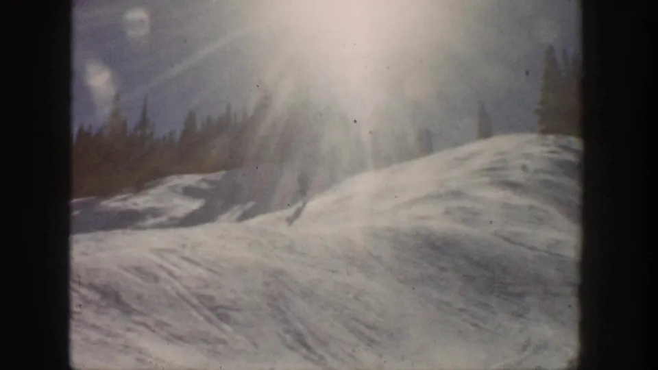 Aspen, Colorado 1961 frame of a snowy hillside, intense sun glare, and evergreen tree line in soft 8mm color.