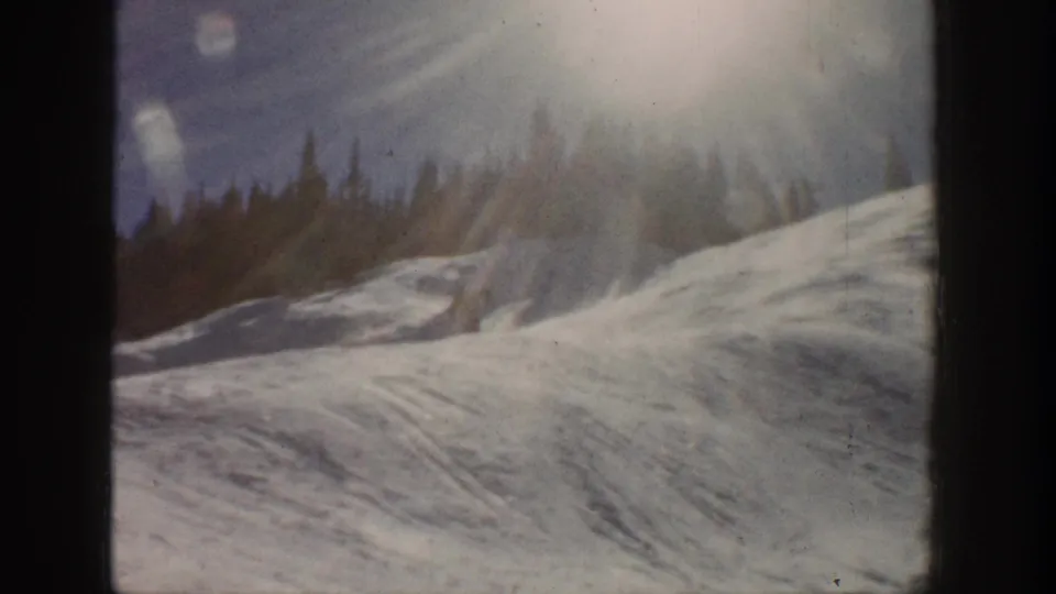 1961 Aspen home-movie view of a winter slope, evergreen trees, and strong sun flare over faded 8mm color.