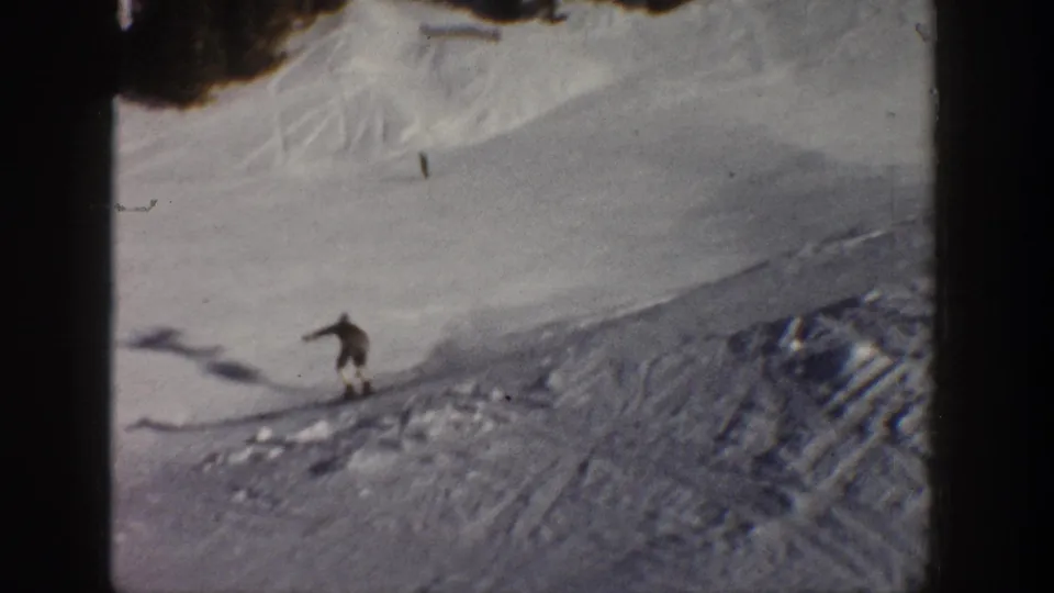 A distant skier descends a snowy Aspen slope in 1961, with ski tracks, tree shadows, and rounded 8mm frame edges visible.