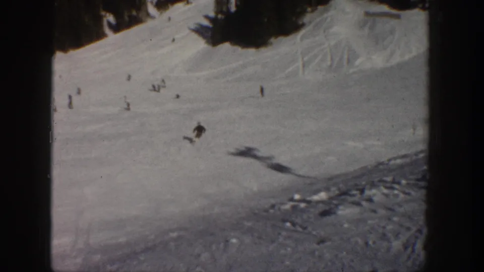 A wide 1961 Aspen ski view shows one skier crossing an open snowfield beneath trees, seen through soft 8mm home-movie footage.