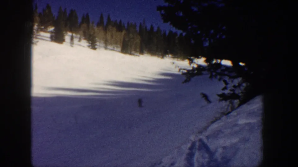 1961 Aspen home-movie frame with a small skier on a snowy mountain slope under a deep blue sky.