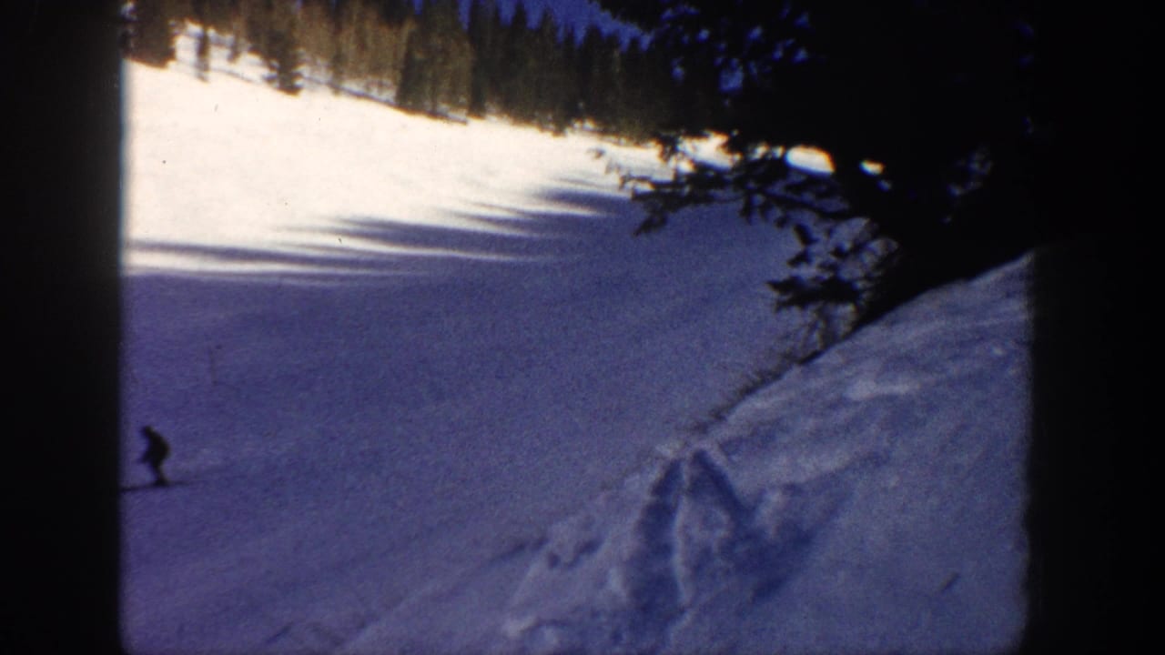 Aspen, Colorado 1961 home-movie frame with a distant skier on a snowfield, framed by dark trees and blue-toned shadow.