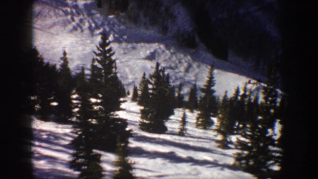 1961 Aspen, Colorado 8mm frame showing a sunlit snow-covered slope with scattered evergreen trees and distant mountain shadow.