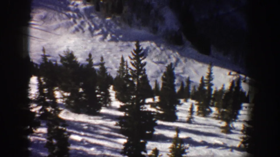 1961 Aspen, Colorado home-movie view of evergreens crossing a bright snowfield beneath darker mountain terrain.