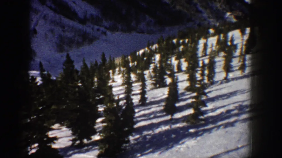 1961 Aspen, Colorado frame with a wooded snowy slope, tall evergreens, long shadows, and soft 8mm color rendering.