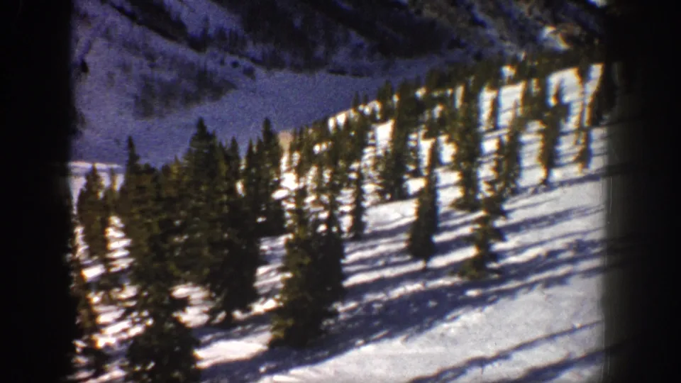 1961 Aspen, Colorado 8mm still showing a bright snowy slope, clustered evergreens, and darkened home-movie frame edges.