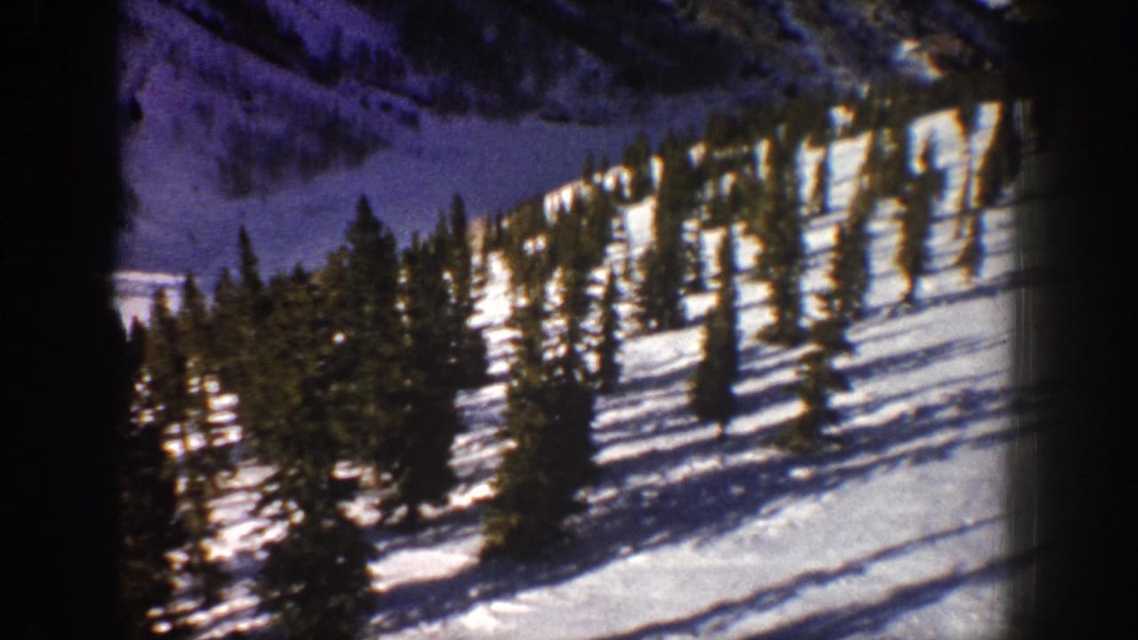 1961 Aspen-area 8mm frame showing a snow-covered alpine slope with scattered evergreen trees and dark frame edges.
