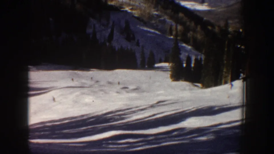 1961 Aspen-area winter frame showing an open snowfield, distant dark trees, and a shadowed mountain slope in the background.