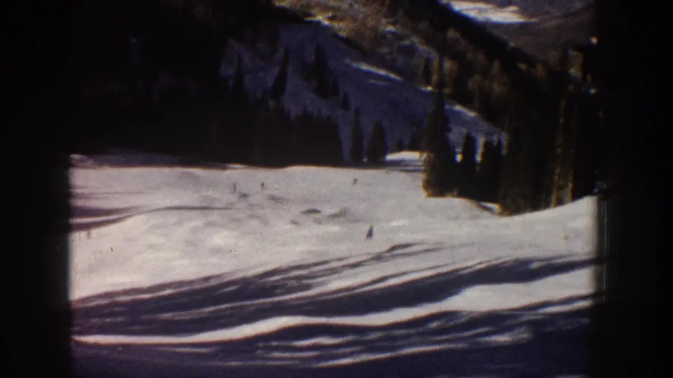 Aspen, Colorado 1961 home-movie still showing distant skiers on a broad snowy run with evergreen trees and strong shadow patterns.