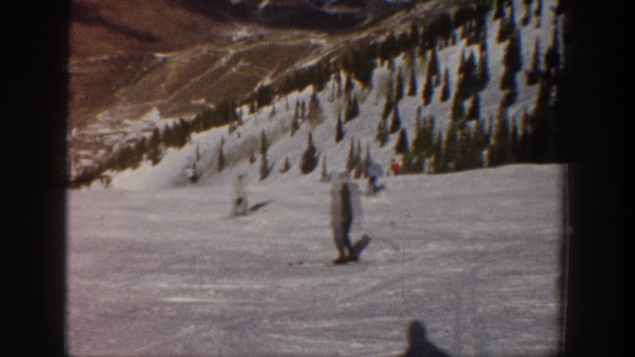 1961 Aspen home-movie frame showing a skier on a broad snowy slope with trees and mountain terrain in the background.