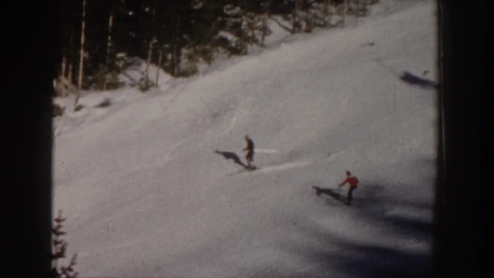 1961 Aspen footage frame with multiple skiers on a bright snowy slope bordered by evergreens, including a figure in red.