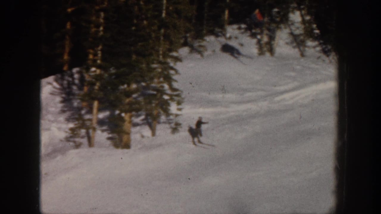 1961 Aspen 8mm frame of a skier descending a snowy run bordered by evergreens and faint tracks.