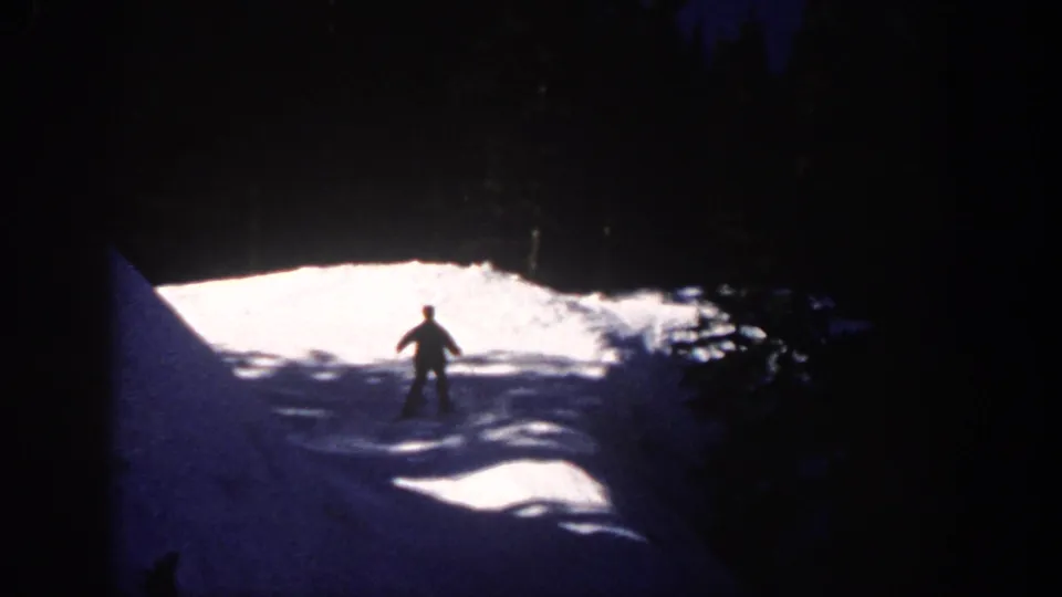 1961 Aspen home-movie frame showing a distant skier silhouetted on a lit snowy slope at night.