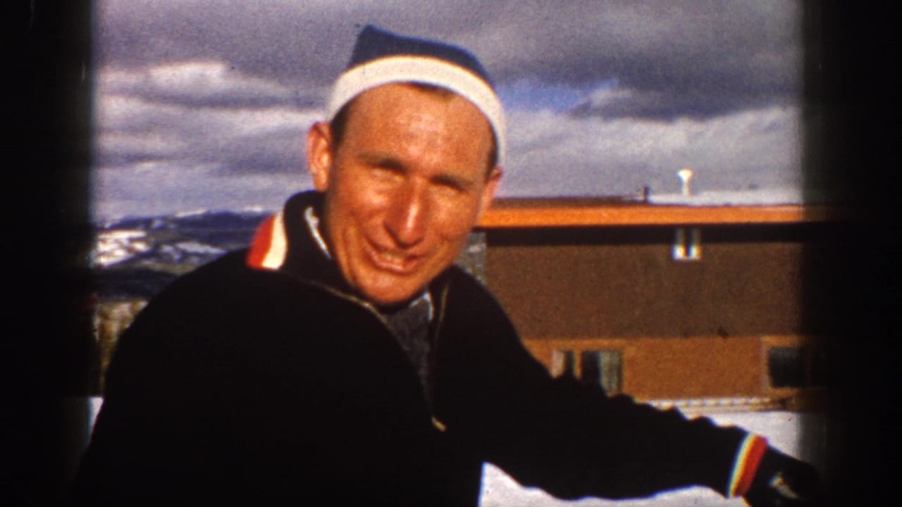 In Aspen, Colorado in 1961, a smiling man in winter clothing faces the camera near snow, a low building, and distant mountains.