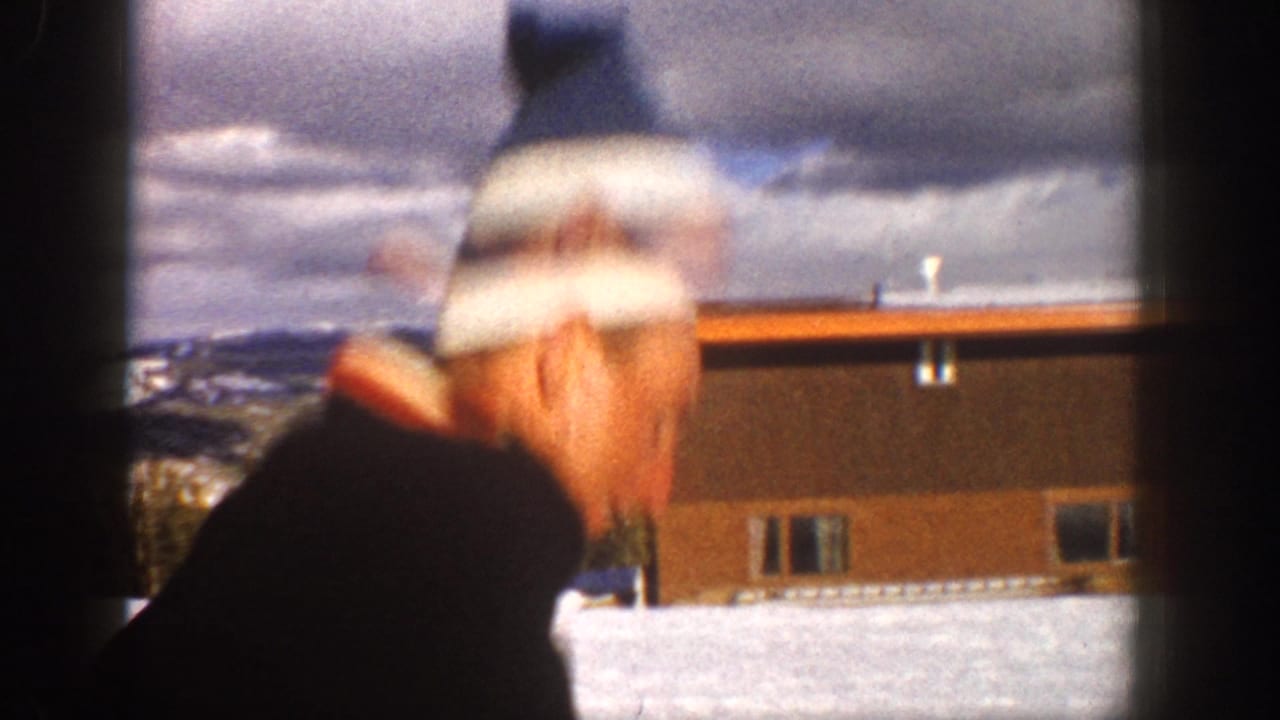The man turns quickly in the 1961 Aspen snow scene, with motion blur, a low building, and mountain ridges behind him.