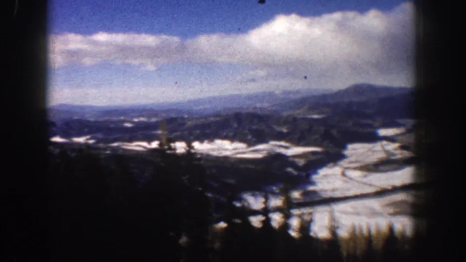 The final frame holds on a 1961 Aspen mountain view with patchy snow, dark foreground shapes, distant ridges, and a clouded blue sky.