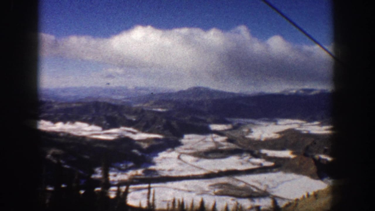 Mountain valley with snow patches, road curves, and lift hardware at the edge.